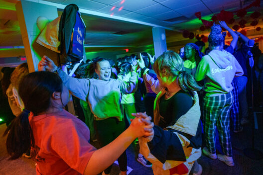 A group of people are dancing energetically in a colorful, well-lit room with a festive atmosphere.
