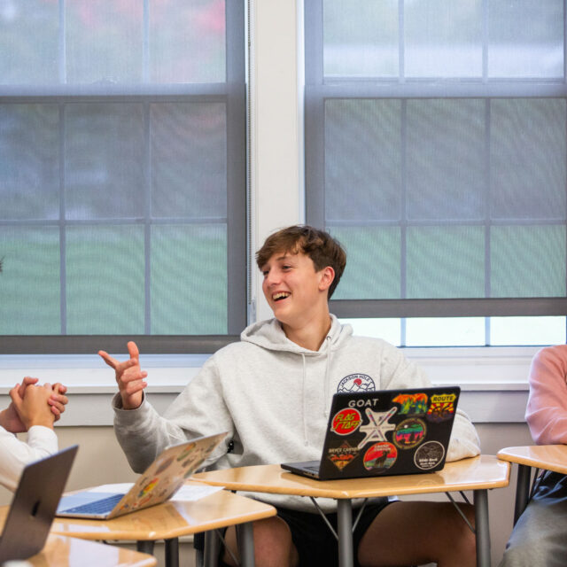 Three students at their desks having a conversation.