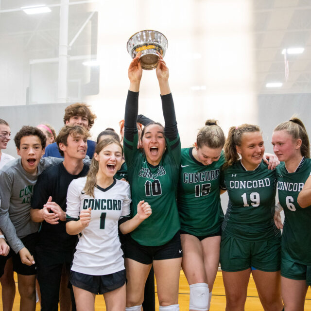 A group of people in sports uniforms celebrate with one person holding up a trophy. The majority wear "Concord" jerseys.