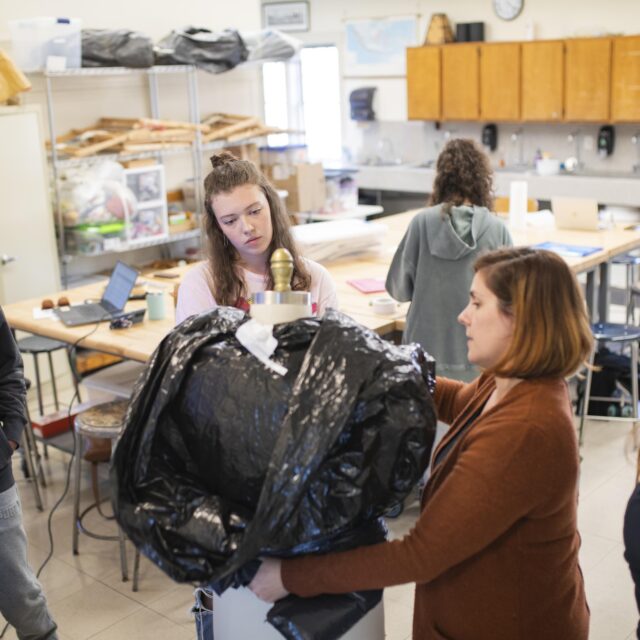 A teacher shows students how to create costume designs in the fiber arts studio.